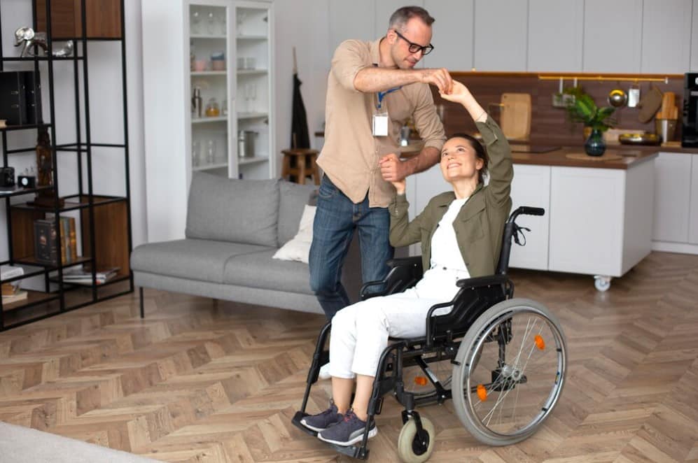 Carer dancing with patient happy in whelchair assisted living