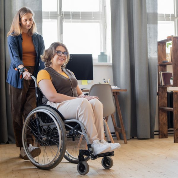 Young,Smiling,Woman,In,Wheelchair,Looking,Forwards,While,Her,Sister